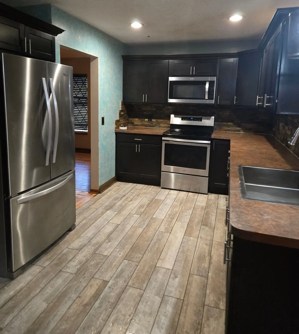 Kitchen with dark cabinets, stainless appliances, an empty sink and tile flooring